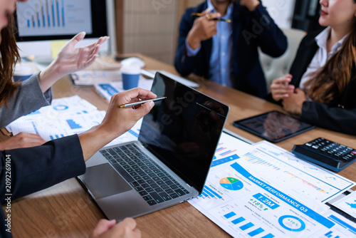 Business people discussing sales charts and financial reports around a laptop in a modern office meeting.