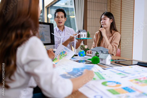 Business team discusses a house model, charts, and plans during a real estate meeting in an office