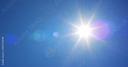 Pan shot of the bright hot summer sun shining in a clear blue sky with beautiful lens flare effects