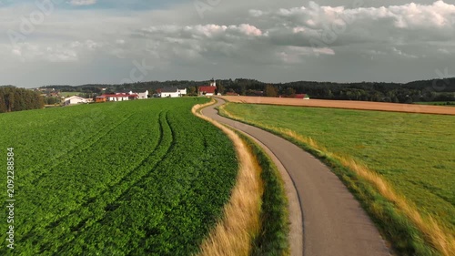 Flying low over a scenic narrow road winding through fields towards a village in a rural area