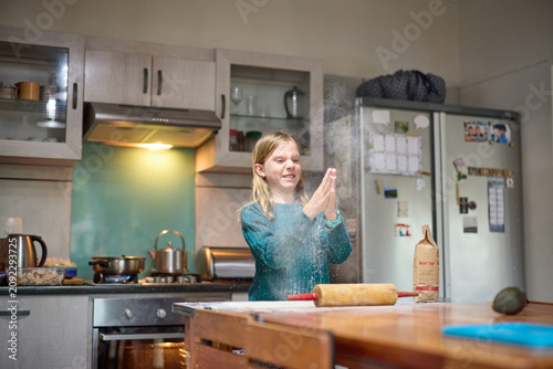 Young girl baking with her grandmother in a sunny home kitchen, clapping flour and laughing