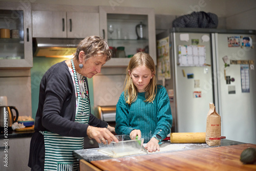 Grandmother teaching granddaughter to bake together in a cozy home kitchen