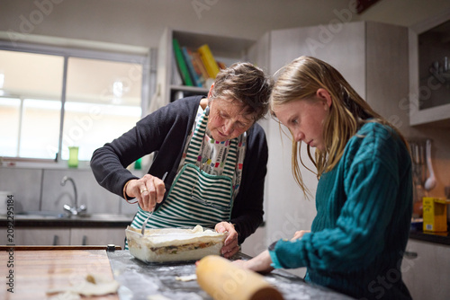 Grandmother teaching granddaughter to bake in a cozy family kitchen, preparing a homemade pie together