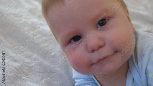 Baby looks at the camera, shallow focus. The infant reaches toward the camera while tossing and turning on the bed
