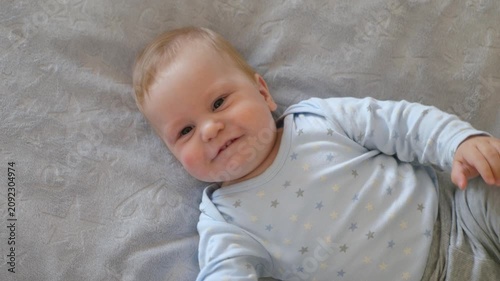 A happy baby waves his arms on a gray fleece blanket. The infant radiates positive emotions and smiles, top view