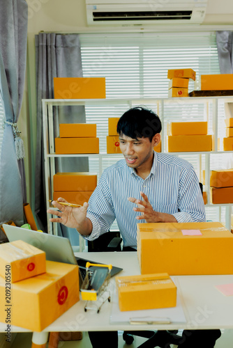 Smiling young Asian male seller live streaming and chatting with customers via computer in home office.