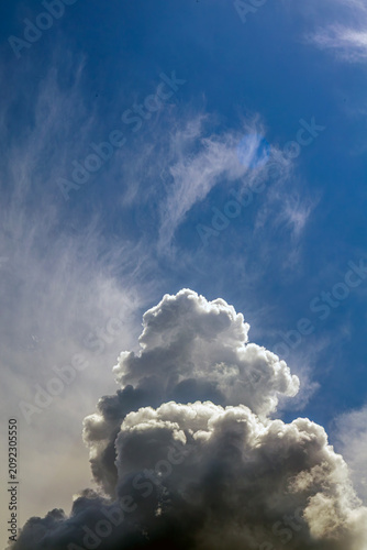 Towering cumulus cloud formation with cirrus layers in blue sky