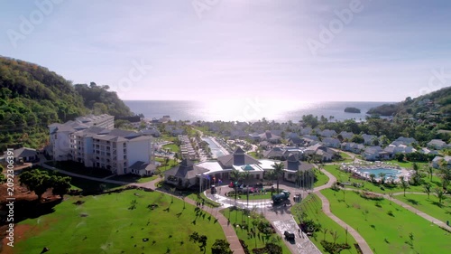 High-angle aerial drone shot capturing a comprehensive view of a luxury Caribbean resort, showcasing villa architecture, extensive landscaped gardens, swimming pools, and the scenic ocean horizon