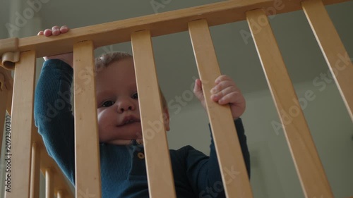 Young child observes and touches crib railing with curiosity. Infant explores playfully, Baby examines nursery surroundings attentively, interacts with crib environment confidently