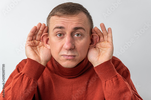 Fotografie Man in a turtleneck sweater cupping his ears with both hands, concentrating and