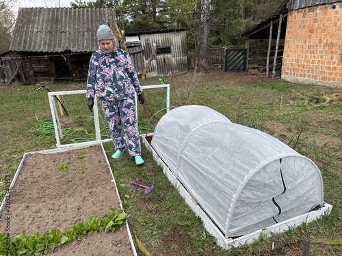 A woman works on a high raised garden bed, which is covered with spunbond over plastic arches.