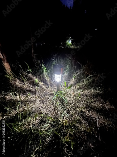 Garden lantern burning in the dark. Rays of light spread across the lawn from the lantern.
