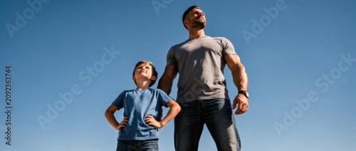 Father and son standing together against clear blue sky, showcasing strength, confidence, and bonding moments during outdoor activities and family adventures.