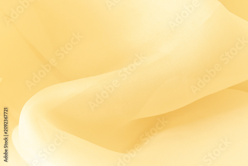 Soft delicate transparent organza, chiffon, silk fabric in pale butter yellow. Close up folds of fabric textile texture as background in champagne gold with copy space.