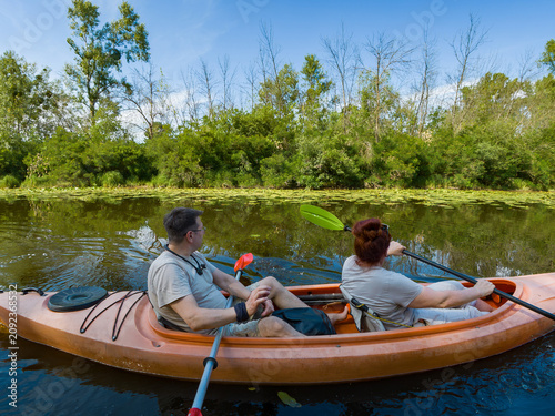 Couple Paddling Orange Tandem Kayak Together on Calm Summer River First-Person View