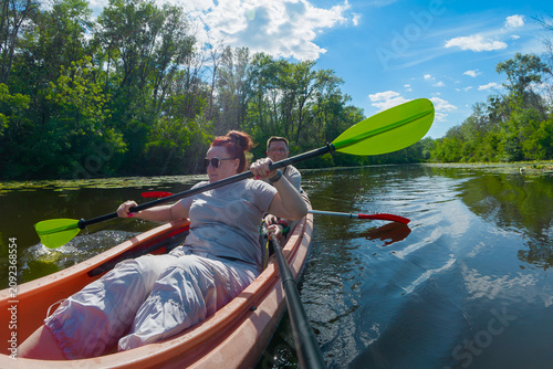 Mature Couple Paddling Orange Tandem Kayak on Calm Forest River During Summer Vacation