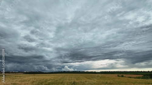Time lapse of heavy dark storm clouds rolling fast across the sky above a vast golden wheat field, creating a dramatic atmosphere before the rain