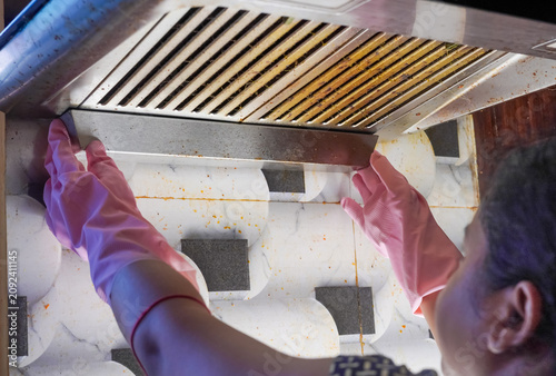 Gloved hand removing dirty cooker hood filter for cleaning or service. Grease and grime buildup requires regular maintenance for modern kitchen appliance hygiene.