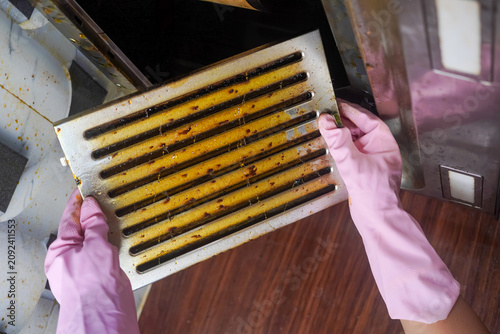 Woman's hand removing a heavily oily dirty filter from cooker hood or kitchen chimney for cleaning or service. Replacing filter in kitchen hood.