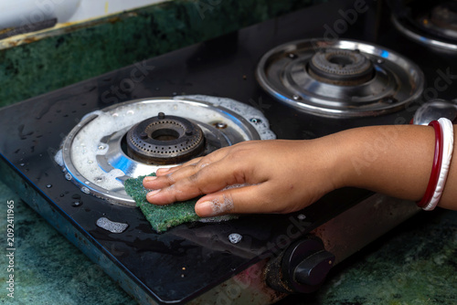 close up of woman hand washes using a green sponge with foam cleaning stainless steel gas stove in the kitchen. ensuring hygienic and cleaning maintenance concept.