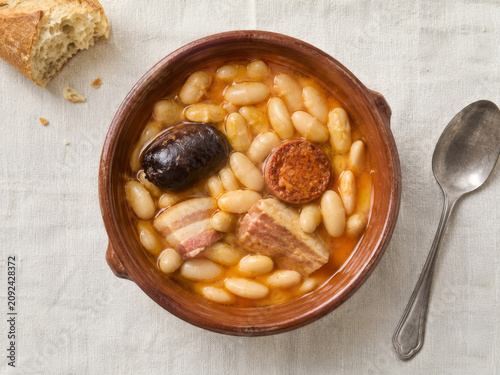 Plato de alubias blancas con embutidos en un tazón de cerámica con pan al lado