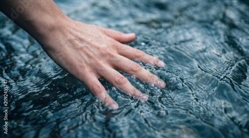 Close up of a female hand gently touching clear cold water in a mountain stream