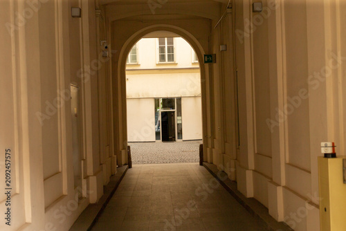 Konstfotografi Long covered corridor with repeating arches and pilasters opening onto a bright cobblestone courtyard