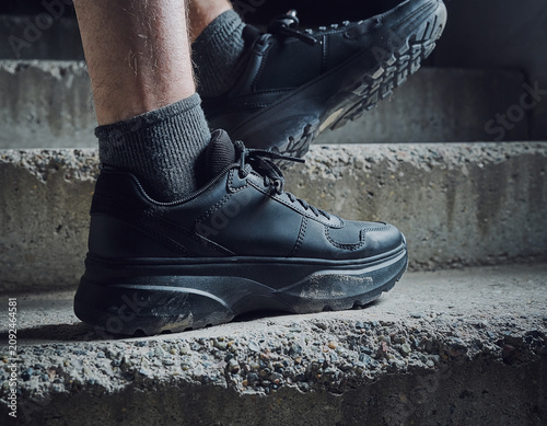 Close-up view of legs and feet on concrete steps in athletic shoes from a low angle in a dimly lit environment with a moody atmosphere