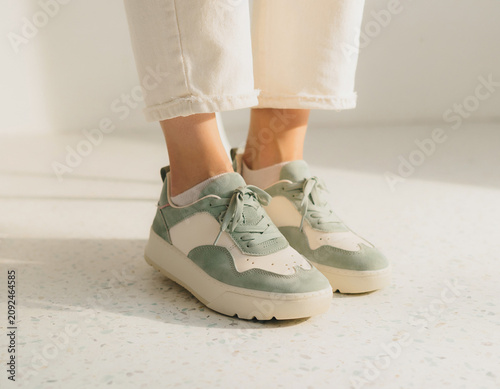 Close-up View of Feet in White Sneakers on Speckled Floor with Sage Accents and Natural Lighting from Above