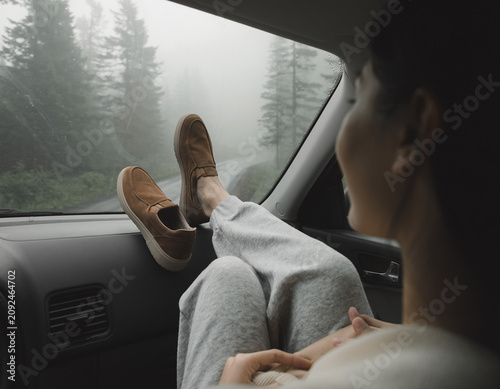 Person gazing out at foggy forest scene from vehicle, feeling serene, with feet on dashboard, in a relaxed atmosphere, enjoying nature, with a calm viewpoint