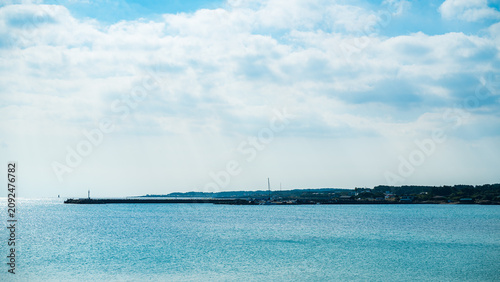 Foto Serene panoramic view of a calm blue ocean and distant breakwater under a vast cloudy sky with gentle sun rays