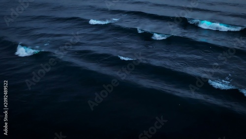Close up aerial view of bioluminescent waves glowing with blue light in the dark ocean water