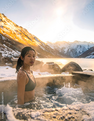Cold-Plunge Wellness Ritual: Serene Asian woman athlete enjoys calm winter cold plunge water recovery ritual near snowy mountain peak during golden sunrise