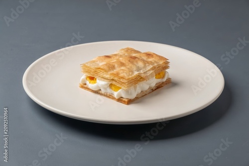 Gibanica on white plate, layered pastry with cheese eggs yogurt, topped with creamy yolk, minimalistic style, dark grey background. Concept of indulgent dessert showcasing flavors.