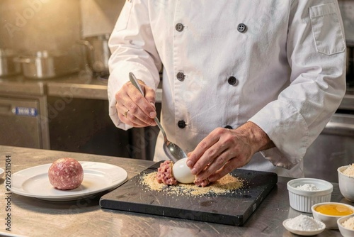 Scotch Egg preparation with sausage wrapped egg with breadcrumbs fried. Concept of culinary excellence in commercial kitchen environment with chef skillfully crafting dishes.