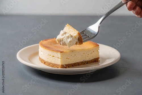 Sernik on white plate, person's hand holding fork. Creamy, light yellow center with flaky crust, topped with whipped cream. Concept of baked cheesecake with twarog vanilla crust.