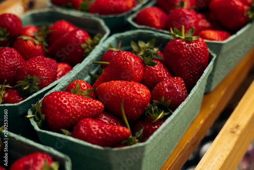 Fresh strawberries displayed in eco friendly paper trays at a farmers market.