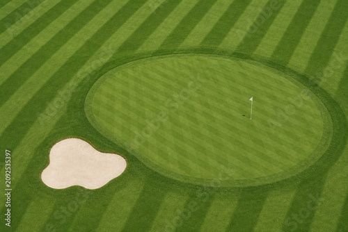 Aerial view of a golf course green showing perfect stripes of dark and light grass.