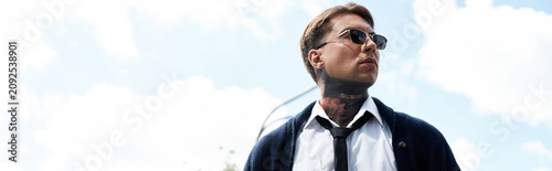 Foto A young handsome man with tattoos poses outdoors wearing sunglasses and a smart