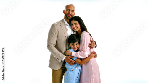 A heartwarming studio portrait of a happy Middle Eastern family of three embracing against an isolated white background. The loving parents and their young son share a serene,