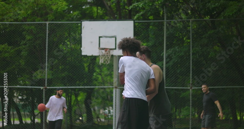 Photos Group of young multiethnic men playing basketball on outdoor court surrounded by