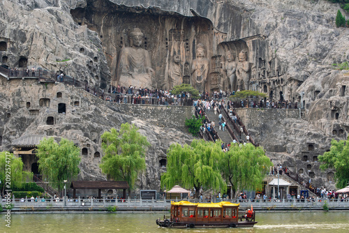 Scenic View of the Monumental Vairocana Buddha at Fengxian Temple in Longmen Grottoes with a Tour Boat on the Yi River at Daytime in Luoyang, Henan, China