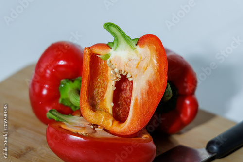 Three juicy red paprika pods on a wooden board. One is cut lengthwise, exposing the seeds and membranes. White background, сlose-up,