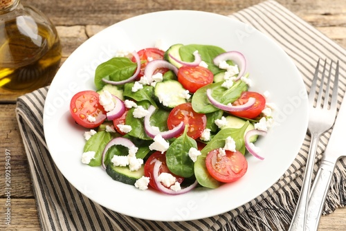Foto Appetizing spinach salad with cheese, walnuts and vegetables served on wooden ta