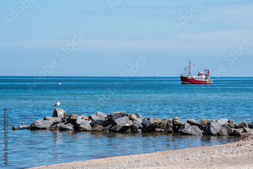 Cuadro en lienzo Red Fishing Boat Navigating in Open Sea Seen From Sandy Beach at Baltic Sea