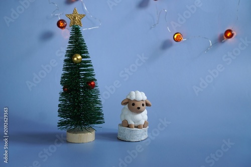 A miniature figure of a vintage sheep symbol of 2027 on a white hemp stands near a Christmas tree on a blue background with garlands in the form of acorns with free space for inserting text