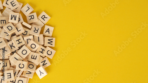 Scattered Wooden Letter Tiles on Yellow Background .