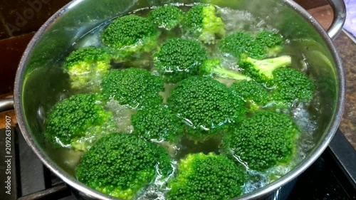 A metal pot of boiling water containing bright green broccoli florets sits on the stove, conveying the impression of a fresh and healthy cooking process.