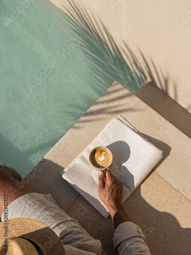 Person enjoying a coffee while sitting by a poolside