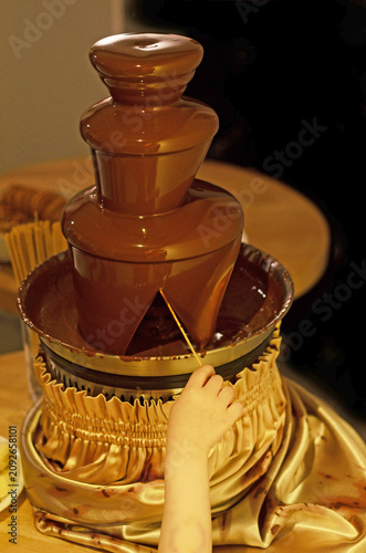 child's hand reaching for flowing chocolate fountain in a celebratory indoor 